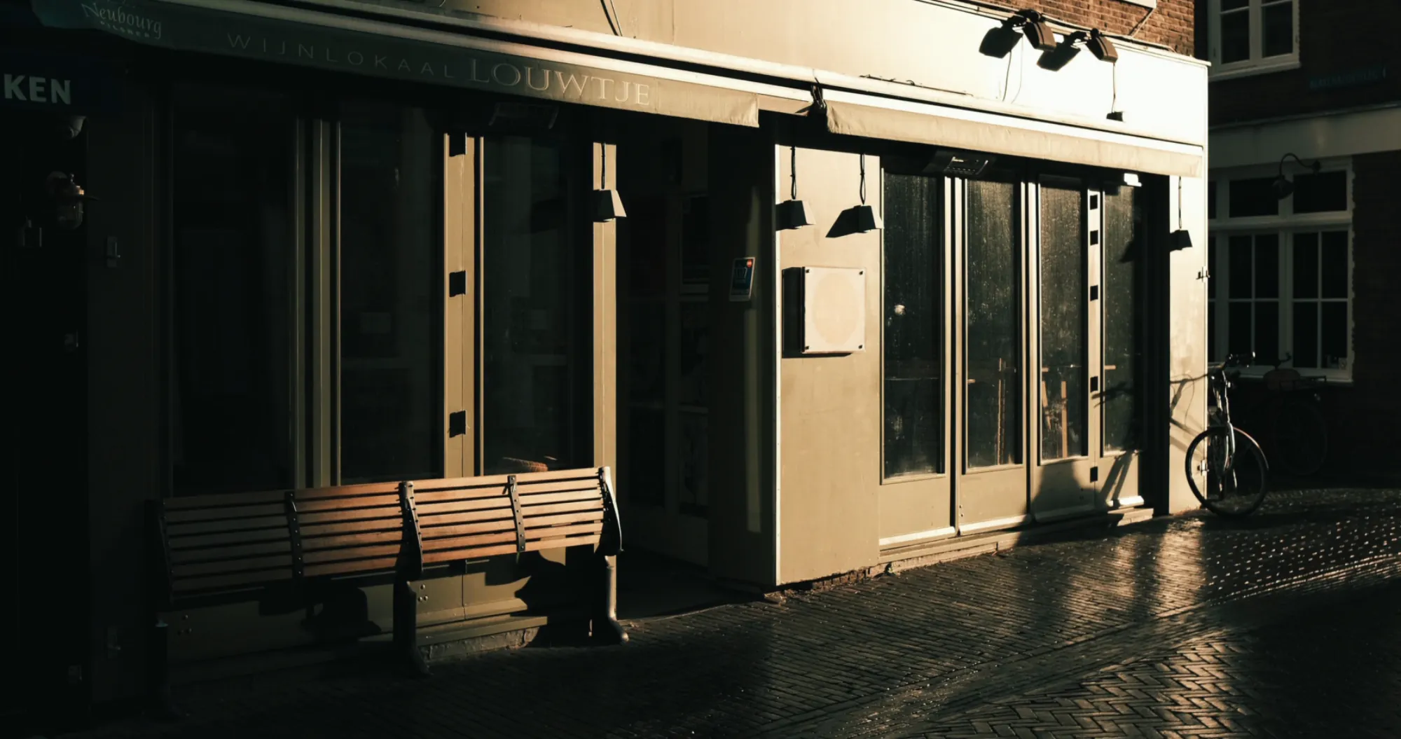 A bench outside a storefront, half in shadow, low sun raking across the street