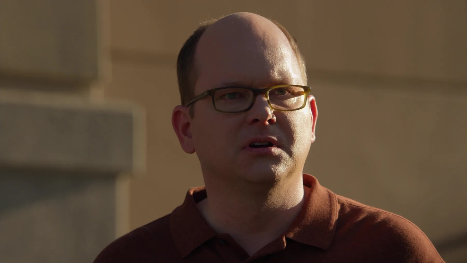 A man in glasses in low golden light, mid-thought