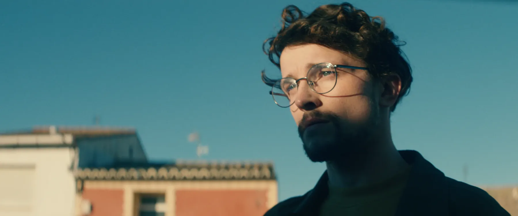 A man in glasses looking up against a clear sky