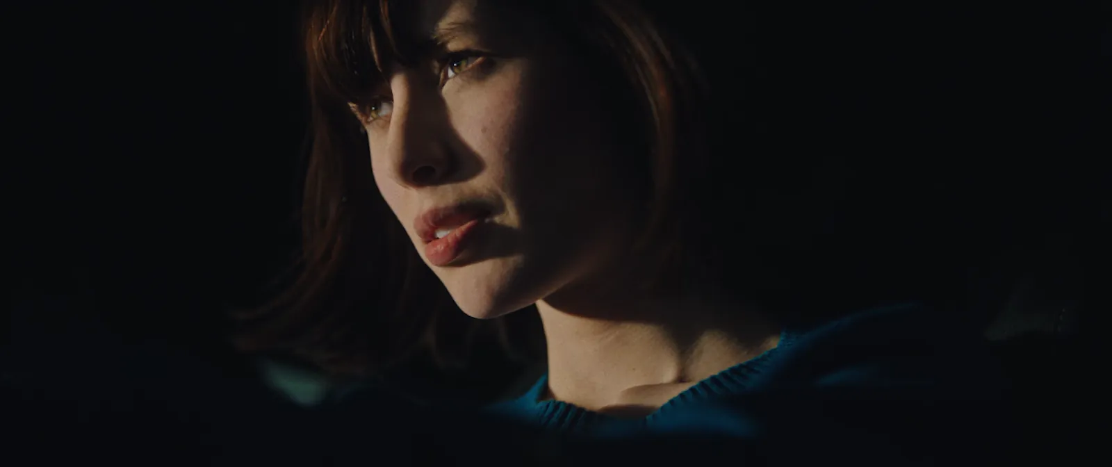 A woman's profile in near darkness with a single warm edge