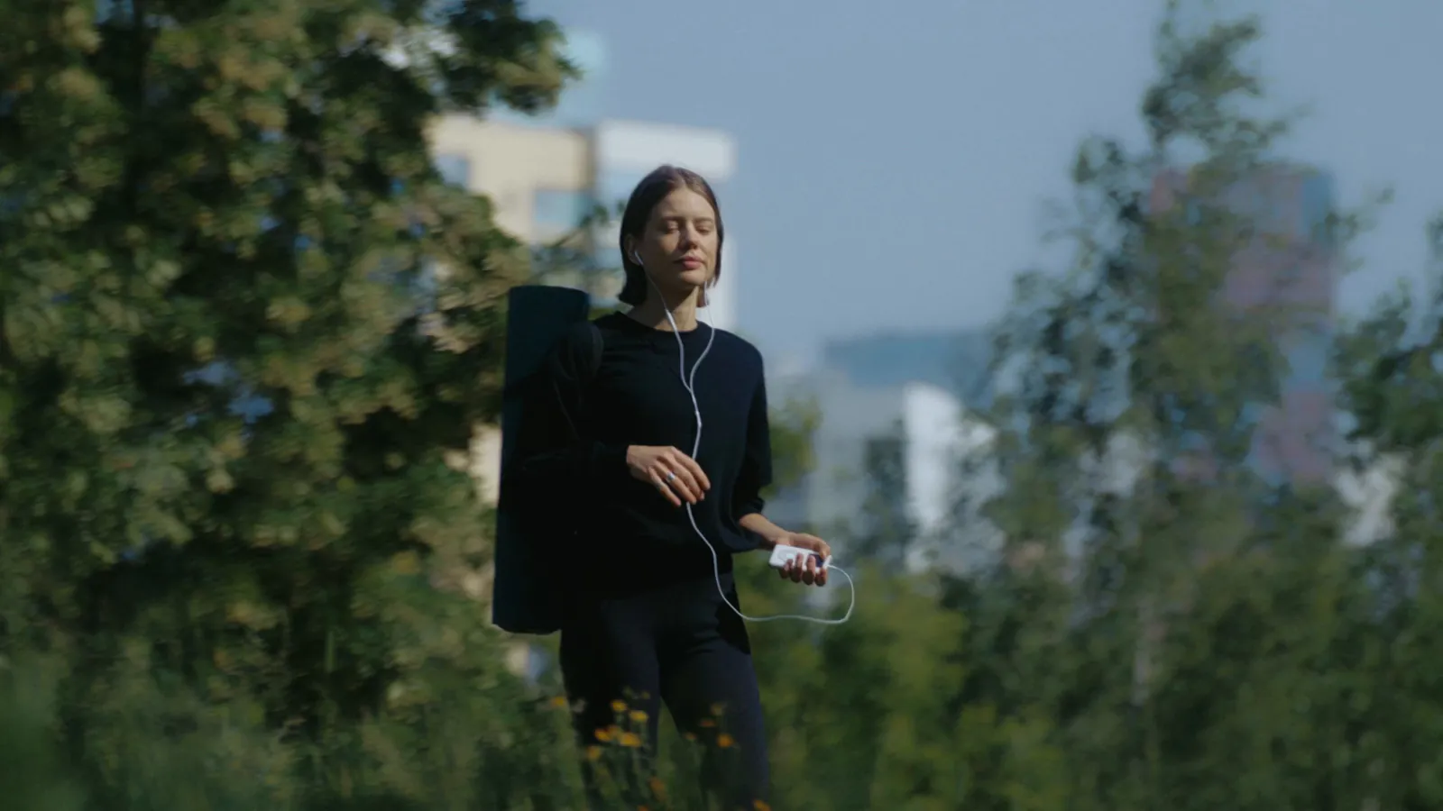 A woman walking with a rolled yoga mat and headphones