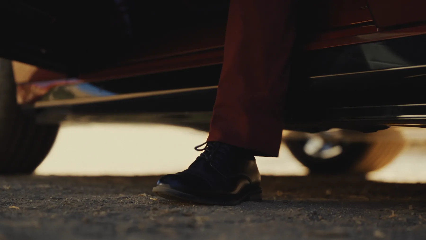A dress shoe stepping out of a car onto the pavement in low sun